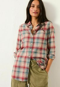 Red and blue plaid button-up shirt in lightweight fabric, featuring a collar, long sleeves rolled at the cuffs, and a relaxed fit.