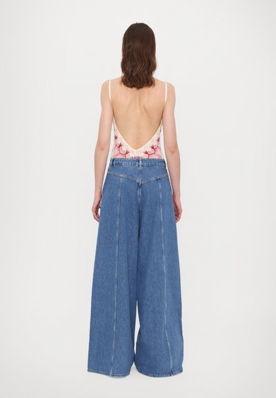Back view of a person wearing a floral low-cut bodysuit and wide-legged blue denim trousers, featuring a clean design and visible stitching.