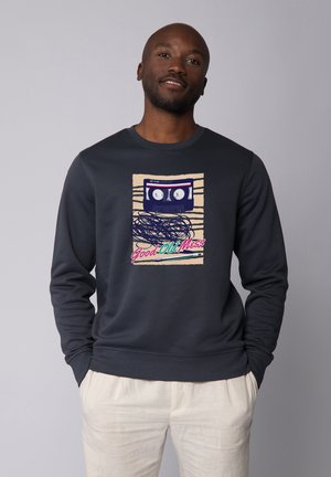 Marineblaues Sweatshirt mit einem Grafikdesign eines blauen Kassettenbandes und buntem Text "Good Old Mess" auf einem beigen Hintergrund, mit gerippten Bündchen und Saum.