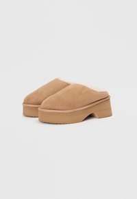 Brown suede clogs with a fluffy white lining, featuring a chunky wooden platform sole, rounded toe, and a smooth texture.