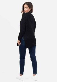 Maglione nero a maniche lunghe lavorato a maglia con un taglio morbido, texture a coste e spacchi laterali, abbinato a jeans scuri e sneakers bianche.