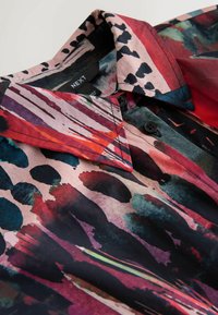 Skjorte krave med sorte knapper, prydet med abstrakt akvarelmønster i røde, pink, sorte og blågrønne toner.