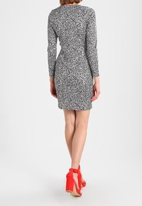 Czarna i biała sukienka w wzory z długimi rękawami, dopasowaną sylwetką i okrągłym dekoltem. Noszona z czerwonymi szpilkami.