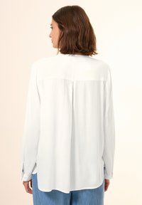 Witte overhemd met lange mouwen en een losse pasvorm, met een effen achterkant, subtiele glans en knoopspecs. Gecombineerd met lichtblauwe jeans.