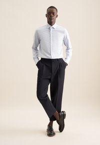 Camicetta blu chiaro con un motivo sottile, abbinata a pantaloni a pieghe blu navy e scarpe stringate nere. Design semplice e sartoriale.