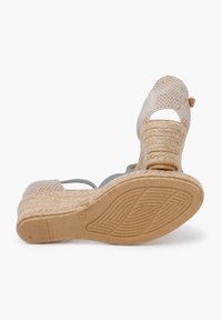 Espadrilky na klínu s tkáněným svrškem v světle béžové barvě, s páskem kolem kotníku a texturovanou podešví z přírodních vláken.