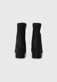Black ankle boots with a zip closure at the back, made of textured fabric, featuring a chunky high heel and a sleek silhouette.