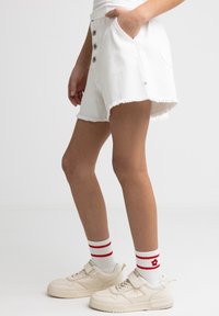 Valged denim lühikesed püksid frakitud ääre, viis nööpi ja küljetaskud, kombineeritud kreemjate tennisetossudega ja triibuliste poolsaapastega.