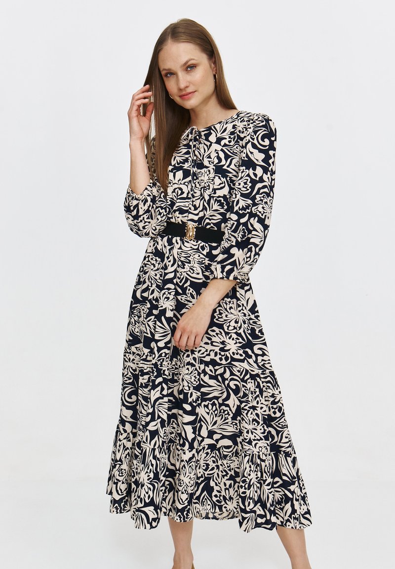 Kwiatowa sukienka midi w kolorze granatowym i kremowym, z długimi rękawami, falbaną u dołu, dopasowaną talią oraz akcentem w postaci złotej klamry.