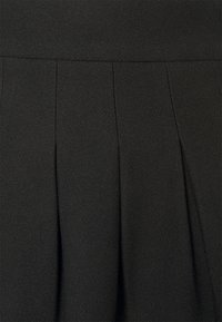 Černá sukně z texturované látky, s plisováními, která dodávají strukturu. Pas má hladký povrch, čímž vytváří štíhlou siluetu.
