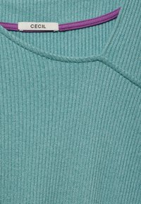 Teal ribbad tröja med rund halsringning, med en lila accent vid kragen. Tyget har ett texturerat mönster. Märke: CECIL.
