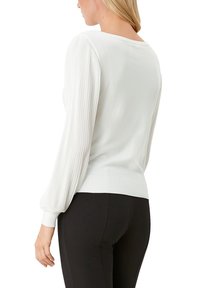 Pull blanc avec manches côtelées bouffantes, encolure ronde et corps cintré, associé à des leggings noirs.