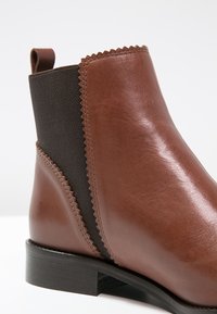 Bottine en cuir marron avec panneau latéral élastique noir, détail de couture en zigzag, languette de tirage et talon bas empilé.