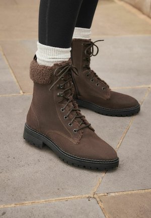 Botas marrones con cordones que presentan un suave puño de piel texturizada, suela de goma, ojales de metal y detalles de costura en contraste.