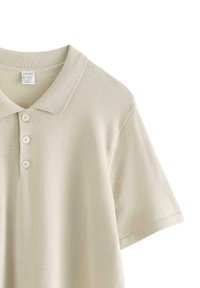 Ljusbeige pikétröja av stickad tyg, med en knapplist med tre knappar, korta ärmar och en klassisk ribbad krage.