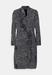 Svart klänning med vita prickmönster, långa ärmar och krage. Har en inslagen design och ett knytband vid midjan. Mjuk tygkänsla.