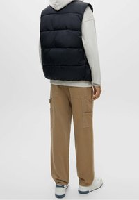 Czarna ocieplana kamizelka na szarym hoodie, w zestawieniu z beżowymi spodniami cargo z kieszeniami. Białe buty z niebieskimi akcentami. Minimalistyczny design.