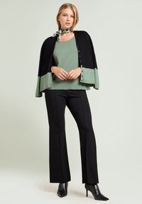 Cárdigan con bloques de color negro y verde sobre una blusa verde claro, combinado con pantalones negros acampanados y tacones puntiagudos negros. Bufanda con patrón circular.