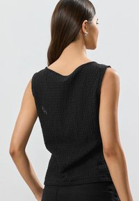 Black sleeveless top with textured fabric, featuring a boat neckline and slightly relaxed fit, visible seam details at the shoulders.