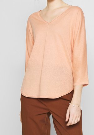 Haut pêche à col en V avec des manches trois-quarts, texture légère, ourlet arrondi et coupe décontractée, associé à un pantalon marron.