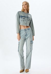 Chaqueta de denim recortada con bolsillos frontales y dobladillo deshilachado, combinada con vaqueros cargo de color azul claro que cuentan con bolsillos laterales y cremalleras.