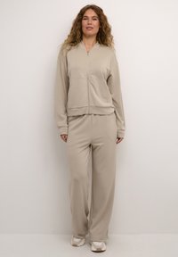 Beige zip-up jacket with long sleeves and matching wide-leg pants, made of soft fabric with a smooth texture, featuring front pockets.