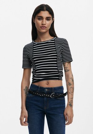 T-shirt cropped à rayures noires et blanches avec des manches courtes, texture côtelée et encolure ronde, associé à un jean bleu foncé et une ceinture noire cloutée.
