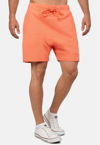 Koraaloranje shorts met een elastische tailleband en trekkoord. Gladde stof, lengte boven de knie, met een discrete geborduurde logo.