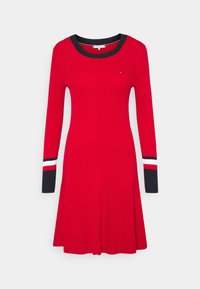 Punainen ribbimekko, jossa on pitkät hihat ja musta kaula-aukko. Hihoissa on raitakuosi mustassa, valkoisessa ja punaisessa. Kahdet hihoista leikkauksen loppuosa on liehuva.