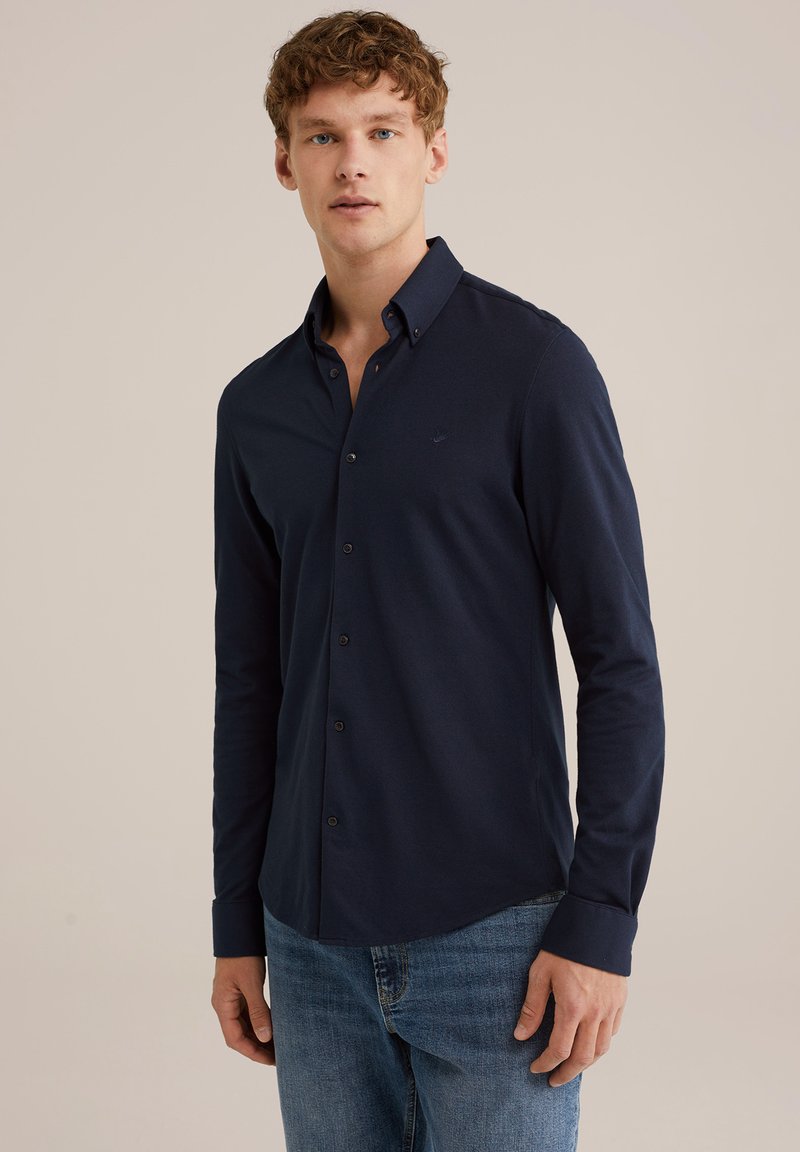 Marineblauwe blouse met lange mouwen en knopen, gemaakt van katoen, met een zachte textuur, op maat gemaakte kraag en een klein logo op de borst. G gedragen met denim jeans.