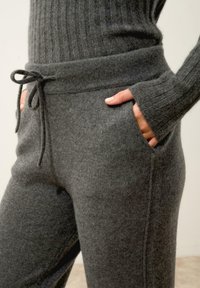 Harmaa neulepusero, jossa on ribbikuvio, pitkät hihat ja korkea pääntie. Yhdistetty harmaisiin naruilla varustettuihin hengittäviin housuihin, joissa on taskut.