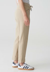 Beige joggings met een koord in de taille, zijzakken en geribbelde manchetten, gecombineerd met witte en marineblauwe sportschoenen. Soepele textuur.