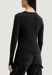 Czarna koszula z długim rękawem o dopasowanym kroju i okrągłym dekolcie. Gładka faktura, bez widocznych wzorów, noszona z ciemnymi spodniami typu cargo.