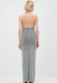 Halternecks Kleid aus silbernem Stoff mit einem rückenfreien Design. Figurbetonte Silhouette, knöchellang mit subtilen Schimmer und einem zentralen Reißverschluss auf der Rückseite.