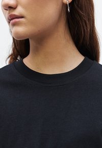 Čierne tričko s okrúhlym výstrihom a krátkymi rukávmi, vyrobené z jemnej bavlnenej látky. Má hladkú textúru a jednoduchý dizajn bez vzorov.