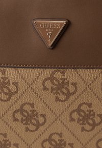 Bolsa Guess castanha com parte superior em couro texturizado e parte inferior em tecido estampado, apresentando letras G e S entrelaçadas.