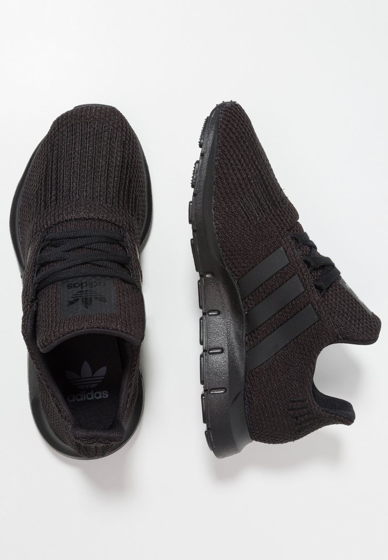 Svarta stickade sportskor med en texturerad ovandel, med tre mörka ränder på sidorna och en svart gummisula.