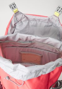 Coral backpack with a gray lining and adjustable straps, featuring divided compartments and a label for names. Smooth, durable fabric.