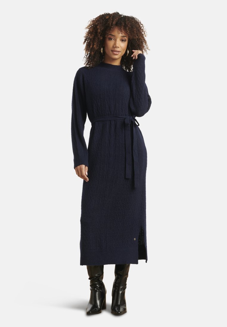 Vestito lungo a maglia blu navy con motivo testurizzato, maniche lunghe, vita con cintura e spacco laterale. Abbinato a stivali neri al ginocchio.