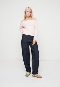 Pulover roz pal cu umerii goi, tricotat cu textură reiată, asortat cu blugi lejeri de culoare albastru închis, având aplicații pe laterale.