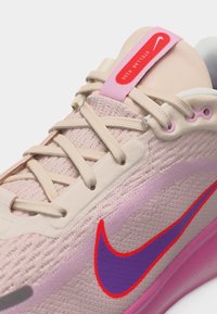 Rosa og beige Nike løpesko med lilla og rød swoosh, beige lisser og rød merkelapp på tungen med teksten "Stellar Ride".