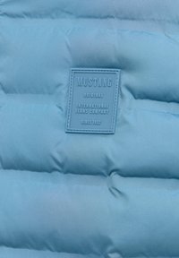 Blauer gesteppten Stoff mit einem aufgenähten rechteckigen Patch, auf dem steht: "Mustang Original International Jeans Company seit 1932."