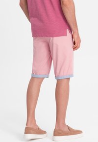 Růžové šortky s ohrnutými světle modrými manžetami, v kombinaci s krátkým růžovým tričkem. Nosené s béžovými slip-on botami. Jednoduchý a neformální design.