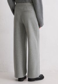 Pantalon à jambes larges en tissu gris clair, présentant un motif à fines rayures subtiles, une taille plate et un détail de poche arrière. Texture lisse.