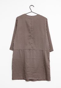 Gemustertes Kleid mit langen Ärmeln, aus leichtem Stoff. Verfügt über dreieckige Formen in Beige und dunklen Farben, hängt an einem Haken.