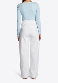 Jasnoniebieska bluzka z długim rękawem i okrągłym dekoltem, zestawiona z białymi, szerokimi spodniami z elastycznym pasem i tylnymi kieszeniami.