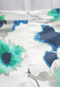 Květinová látka v odstínech zelené, modré a šedé na bílém pozadí. Na zadní straně je skrytý zip.