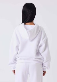 Witte oversized hoodie met een trekkoordcapuchon, zachte stof, verlaagde schouders en geribbelde boorden. Eenvoudig ontwerp zonder zichtbare patronen.