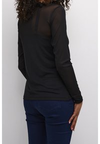 Haut noir à manches longues avec un dos transparent, une texture lisse et une coupe ajustée. Associé à un jean bleu foncé présentant une coupe décontractée.