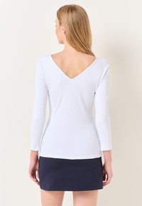 Biała bluzka z długim rękawem o ribbowanej strukturze i głębokim dekoltem na plecach, połączona z ciemnoniebieską spódniczką mini. Gładki materiał, dopasowany krój.